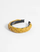 Vincha color mostaza de cuero sintético con diseño trenzado en la parte superior.