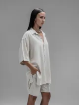 Camisa de corte oversize en color beige, confeccionada en tejido de lino y algodón. Presenta cuello clásico, cierre frontal con botones y mangas cortas amplias.