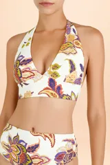 Top de bikini estilo halter con escote profundo y banda ancha bajo el busto. Presenta un diseño estampado con motivos botánicos y paisley en tonos cálidos y púrpura sobre fondo blanco.