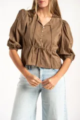 Blusa blanca de algodón con delicado bordado floral, mangas abullonadas de largo 3/4 y cierre frontal con botones y cordón ajustable en la cintura.