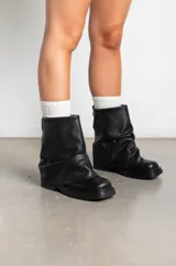 Botas de cuero negro con caña media y diseño holgado con efecto fruncido en la parte superior. Presentan una suela plana con taco bajo y puntera redondeada.