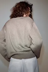 Sweater de punto grueso color beige, con cuello en V profundo y mangas largas. Cuenta con terminaciones acanaladas en el cuello, los puños y el ruedo.
