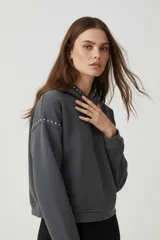 Canguro gris oscuro con capucha y cuello alto, decorado con tachas metálicas plateadas en los hombros y el cuello. De corte holgado y manga larga.