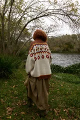 Buzo de punto grueso con cuello alto y diseño jacquard que presenta motivos de granjeros, casas y árboles en tonos crema, marrón, rojo y amarillo.