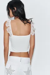 Top corsetero blanco con escote cuadrado y tirantes anchos con volados de encaje. Presenta costuras marcadas y cierre frontal con ganchos metálicos.