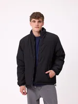 Campera reversible de nylon con cuello alto y cierre frontal. Un lado es de color gris liso con logo bordado, mientras que el otro lado presenta un estampado abstracto en tonos azules. Cuenta con bolsillos laterales y puños elásticos.