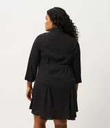 Vestido corto tipo chemise de poliéster con estampado de lunares, cuello camisero con botones frontales, mangas largas con puños elásticos y lazo ajustable en la cintura.