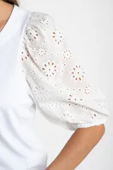 Remera de algodón color rosado con mangas cortas abullonadas de broderie con diseño floral calado. Presenta cuello redondo y costura vertical central en el frente.