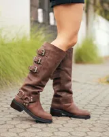 Botas de caña alta confeccionadas en cuero color marrón caoba. Presentan un diseño robusto con tres hebillas metálicas ajustables en el lateral superior y una correa con hebilla y remaches metálicos en la zona del tobillo. Cuentan con un taco bajo cuadrado y suela de goma resistente.