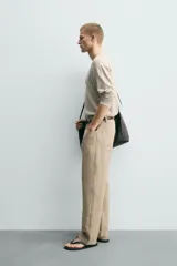 Jersey de punto de corte relajado, con cuello redondo amplio y mangas largas. Presenta un diseño de rayas horizontales finas en contraste sobre fondo beige.