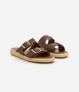 Sandalias marrones con dos tiras anchas con hebillas plateadas y suela plana con textura de rafia.