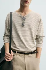 Jersey de punto de corte relajado, con cuello redondo amplio y mangas largas. Presenta un diseño de rayas horizontales finas en contraste sobre fondo beige.