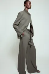 Pantalón de tiro alto con corte ancho y pernera recta. Presenta raya planchada en el delantero, bolsillos laterales y cierre frontal con cremallera y ganchos metálicos. Incluye un cinturón fino en tejido a contraste.