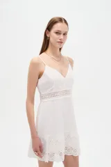 Vestido corto blanco de algodón con diseño de broderie, escote en V y tirantes finos. Presenta detalles de encaje y botones frontales.