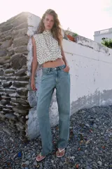 Blusa sin mangas blanca con estampado de lunares negros, cuello alto drapeado y nudo frontal en el bajo.