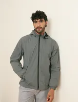 Campera impermeable gris con capucha, cierre frontal y bolsillos laterales con cremallera.