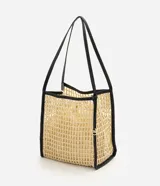 Cartera tipo shopper confeccionada en paja trenzada de color beige con detalles en negro, asas de hombro de poliuretano y compartimento interior con cierre de cordón ajustable.