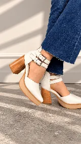 Zapatos de tacón alto blancos con plataforma y taco grueso efecto madera, puntera redondeada, diseño cerrado en la parte delantera y doble tira con hebillas metálicas en el tobillo.