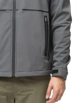 Campera softshell negra con capucha ajustable, cierre frontal completo y bolsillos laterales con cierre. Presenta puños con ajuste de velcro y logo de la marca estampado en el pecho.