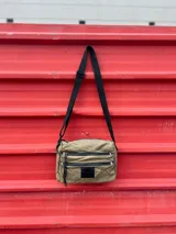 Bandolera verde de nylon con correa negra regulable y múltiples bolsillos con cierre.