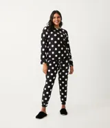 Pijama de dos piezas con estampado de lunares blancos sobre fondo negro. Incluye una blusa de manga larga con cuello redondo y un pantalón largo con cintura elástica y cordón ajustable.