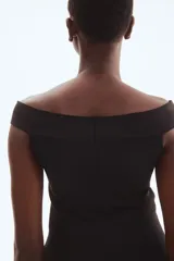 Top largo de punto tupido, color negro, con hombros descubiertos, corte ajustado y diseño acampanado estilo peplum desde la cintura.