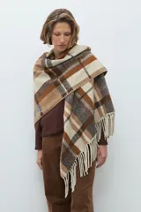 Ruana de tejido grueso con diseño de cuadros en tonos beige, marrón y gris, con terminación de flecos en los bordes.