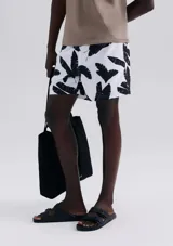 Short de baño blanco con estampado de hojas negras, cintura elástica y bolsillos laterales.