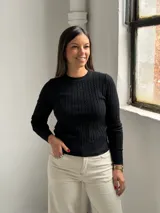 Sweater de punto negro con diseño de trenzas verticales, cuello redondo y mangas largas ajustadas.