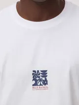 Camiseta blanca de corte oversize, confeccionada en algodón orgánico de alto gramaje. Presenta un diseño gráfico estampado en el centro del pecho con el logo de la marca.