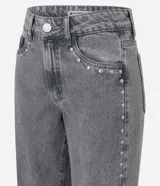 Pantalón de jean color gris lavado, con corte wide leg de piernas amplias y cintura baja. Presenta detalle de tachas metálicas a lo largo de las costuras laterales, cierre frontal con botón y bolsillos funcionales.
