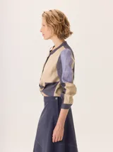 Camisa de algodón color gris claro, con cuello mao, cierre frontal de botones y mangas largas. Presenta un estampado sutil de hojas y flores, y detalles de bordado calado en los hombros.