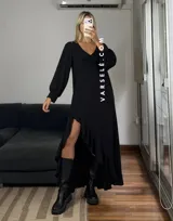 Vestido largo color marrón, con escote en V, mangas largas con puños y detalle de encaje en el pecho. Presenta un diseño asimétrico con volados en el ruedo y una abertura frontal.