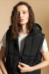 Chaleco acolchado de nylon color negro, con diseño capitoneado, capucha integrada y cierre frontal con tirador metálico.
