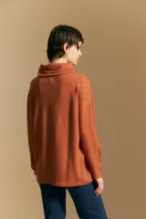 Polera de tejido de punto color naranja con cuello alto de caída relajada y diseño de líneas en relieve. Presenta una silueta holgada con hombros caídos y mangas largas.