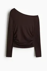 Remera de manga larga color marrón oscuro, con escote asimétrico que deja un hombro al descubierto. Presenta frunces laterales que generan un efecto drapeado en el torso.