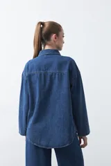 Sobrecamisa de jean negra de silueta relajada, con tachas aplicadas en líneas orgánicas que recorren la prenda. Tiene cuello camisero, cierre frontal con botones a presión y mangas largas.