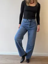 Pantalón de jean corte mom fit con tiro alto, confeccionado en denim de lavado clásico. Presenta cierre frontal con botón y cierre metálico, con bolsillos funcionales delanteros y traseros.