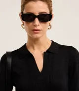 Blusa de punto ajustada color negro, con cuello polo y escote pronunciado en V. Presenta un tejido acanalado vertical en el torso y mangas largas.