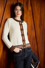 Cardigan de punto color crudo con detalles en marrón y negro. Presenta cuello redondo, cierre frontal con botones forrados y puños acanalados con rayas horizontales.