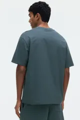 Remera verde oscuro de corte relajado, confeccionada en punto de algodón de peso medio, con cuello redondo ribeteado y hombros caídos.