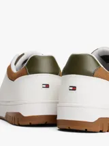 Zapatillas de corte bajo estilo retro baloncesto, confeccionadas en piel blanca con paneles de textura a contraste en color marrón y verde oliva en el talón. Presentan suela de goma dentada, cierre con cordones y logo de Tommy Hilfiger en el lateral y la lengüeta.