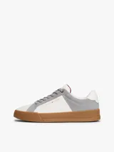 Zapatillas de tenis Tommy Hilfiger de corte bajo, confeccionadas en piel nobuk con paneles de texturas mixtas en blanco y gris. Presentan suela de goma color caramelo, cierre con cordones y detalles distintivos de la marca en la lengüeta, lateral y talón.