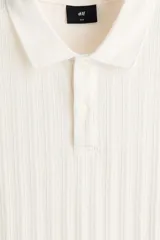 Remera polo de manga corta en punto texturizado de peso medio, color blanco, con cuello, tapeta de botones y bajo recto. Corte ajustado que realza el contorno del cuerpo.