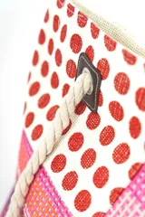 Bolso tipo tote con diseño de paneles en bloques que combinan estampado de lunares rojos sobre fondo blanco y franjas horizontales en tonos rosados, naranjas y morados. Cuenta con asas de soga gruesa de algodón en color crudo, sujetas con ojales metálicos y refuerzos de cuerina marrón.