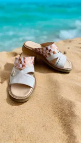 Sandalias de cuero blanco con tiras cruzadas, plataforma baja con suela de caucho y detalle pintado a mano en tonos cobrizos y blancos en la parte superior.