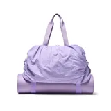 Bolso deportivo de gran capacidad en color lila, confeccionado en material textil con acabado arrugado. Cuenta con doble asa superior, correa ajustable y desmontable, y compartimento principal con cierre doble. Incluye correas en la base para sujetar accesorios y una bolsa interior desmontable.