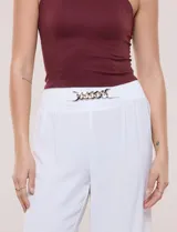 Pantalón negro de calce relajado y caída fluida, confeccionado en poliéster con textura de crepé. Tiene cintura alta elastizada estilo pull on con un aplique de cadena metálica decorativa, y pierna de corte ancho tipo wide leg corto por arriba del tobillo.