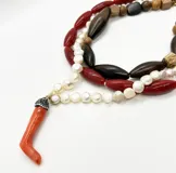 Collar de tres hilos con cuentas de resina rojas, perlas de vidrio blancas y cuentas de madera en tonos marrones. Incluye un dije colgante en forma de coral rojo.