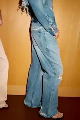 Jeans de corte boyfriend y tiro medio, con diseño de cinco bolsillos, cierre frontal con cremallera y botón metálico. Presenta un acabado lavado con detalles de roturas y desgastes.